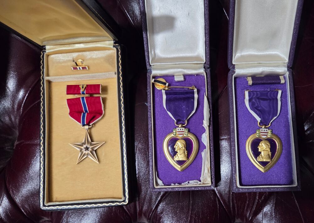 Three cased medals on oxblood leather: the Bronze Star with its V device, and two Purple Hearts
