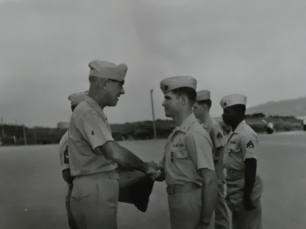 Black-and-white photograph: Lieutenant Himes, at attention in khaki service uniform, shakes hands with a senior Marine officer at an outdoor award ceremony, other Marines in line beside him