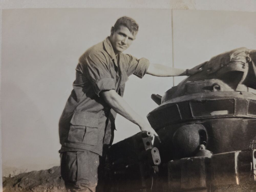 Young Harris Himes in combat fatigues beside an M48 tank, his hand on the gun mantlet